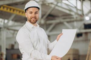 Smiling engineer holding blueprint in modular building factory photo