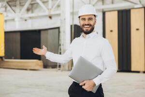 Smiling architect showing building under construction with laptop in hand photo