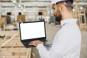 Architect using laptop with blank screen in modular building factory photo