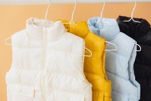 Four sleeveless jackets hanging on hangers presenting different colors photo