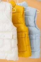 Sleeveless down jackets hanging on hangers on orange background photo