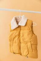 Mustard yellow vest with faux fur collar hanging on clothes rack photo