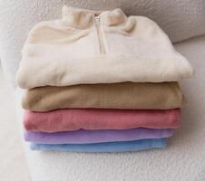Stack of colorful fleece jackets on white sofa photo
