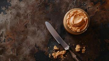 Top-down view of jar of hazelnut spread next to spreading knife on wooden table, culinary photography photo