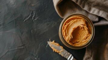 Top-down view of jar of hazelnut spread next to spreading knife on wooden table, gastronomy photography photo