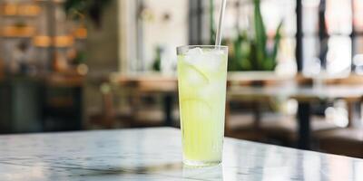 Tall glass with a straw, containing a light green liquid, placed on a marble table, food setting photo