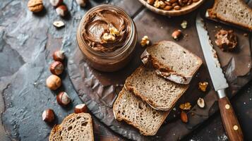 Open jar of hazelnut spread next to sliced loaf of bread and knife, meal photography photo