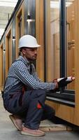 A worker is applying polyurethane foam to fill gap between sash and window frame in prefabricated modular house. Vertical video