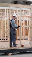 Worker carpenter assembling a modular house. Vertical video