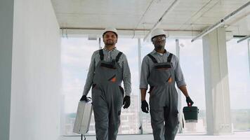 Indian and African construction workers in uniform and helmets walking with tools on construction site video