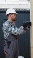 Worker using drill and working on building development of prefabricated home. Process of construction modern modular house in factory. Vertical video