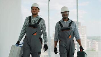 Two diverse construction workers in uniform and helmets walking with tools on construction site video
