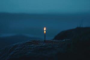 A Single Candle Burning Brightly on a Rocky Outcrop at Dusk photo