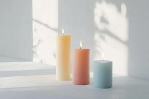 Three Burning Candles in Different Colors on a White Surface with Light Patterns photo