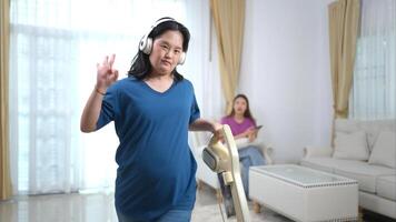 A sister happily cleans the house with headphones on while her sister works on the sofa in the living room at home during the holidays photo