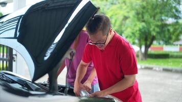 A brother and sister help each other execute a basic engine check on their parents' automobile photo