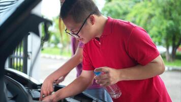 A brother and sister help each other execute a basic engine check on their parents' automobile photo