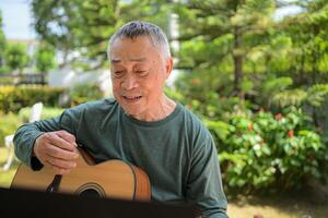 Senior man a veteran guitarist plays music in the garden at home photo