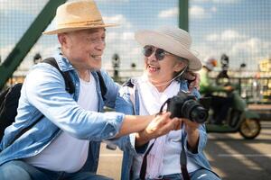 An elderly couple relaxes and looks at photos in camera after walking through the city streets with the road and bridge structures in the background