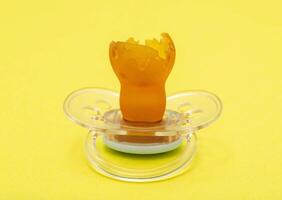 Low-quality torn baby silicone pacifier on a yellow background, close-up. Concept of the anatomical shape of the pacifier, teething in children. photo