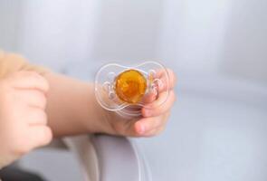 The baby is holding a torn and chewed silicone pacifier in his hands. Concept of teething in children, sucking reflex. Copy space for text photo