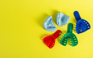 Blue plaster cast of a dental jaw and a dental tray for an impression of a dental jaw on a yellow background. The concept of orthodontics in dentistry, the manufacture of dentures and crowns. photo