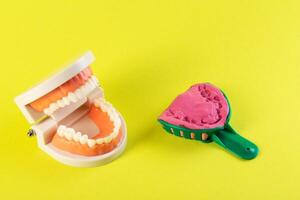 Green dental spoon for taking a dental impression in a mock-up of a dental jaw on a yellow background. Making an artificial jaw for malocclusion. Manufacturing of dental prostheses photo