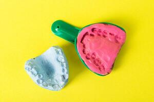 Dental spoon with alginate plastic mass for taking an impression of the dental jaw on a yellow background. Blue plaster dental jaw on a yellow background. Orthodontics in dentistry photo
