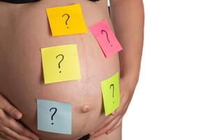 Multi-colored stickers with a question mark are glued on the belly of a pregnant girl. The concept of the uncertainty of the birth of a boy or girl. Copy space for text photo