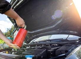 The driver of the car directs a powder fire extinguisher at the engine compartment of the car in which there is fire and smoke. Car fire, background. Electrical short circuit photo