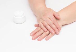 The hands of an elderly woman on a white background and a complex cream with vitamin against wrinkles and tightness on the skin of the hands, restoring the epidermis photo