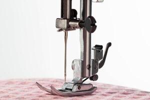 A needle with a needle holder and a sewing machine foot on a background of pink fabric. Macro, industry. Copy space for text. Tailoring services photo