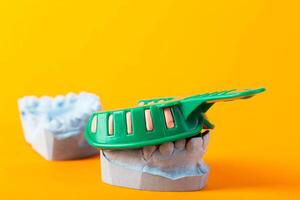 Green dental impression tray on a blue plaster jaw of a patient on a orange background. The concept of taking an impression of the jaw for the manufacture of crowns and dental prostheses. photo