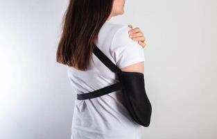 A girl on a white background with a black supporting medical bandage after a dislocation of the shoulder joint and a bone fracture. Rehabilitation after injury, orthopedics and traumatology photo