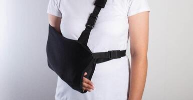 A girl in white with a fixing black bandage on her arm after an injury, a fracture of the radius and a sprain. Arm support bandage, hand immobilization photo