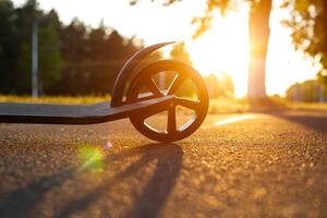 Part of the scooter and the rear wheel close-up against the background of a sunset in the summer. The concept of innovation and development in the scooter rental business. photo
