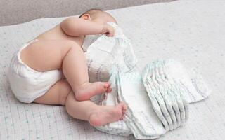A little caucasian baby boy in a diaper lies on a white background and plays with a bunch of diapers. Copy space for text photo