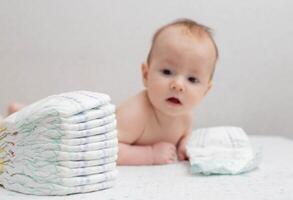 A little boy at the age of 5 months lies in a diaper on a white background and looks at the camera. Stack of diapers, anti-leak, soft and comfortable. Copy space for text photo