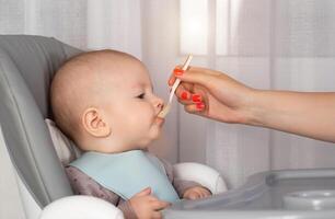 A mother feeds porridge from a spoon to a little boy who is 8 months old. Feeding infants. Copy space for text photo