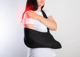 A girl on a white background with a black supporting medical bandage after a dislocation of the shoulder joint and a bone fracture. Rehabilitation after injury, orthopedics and traumatology photo