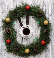 Christmas clock made of fir branches, clock hands of pine nuts, a cup of coffee and Christmas toys on a white wooden background, clock photo