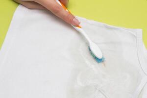 Girl cleans the stain on the child's shirt with a brush using a stain remover, close-up, whitener, hand photo