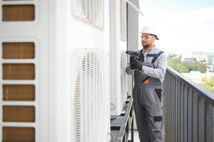 Indian Repairman in uniform installing the outside unit of air conditioner photo
