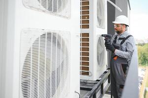 Indian Repairman in uniform installing the outside unit of air conditioner photo