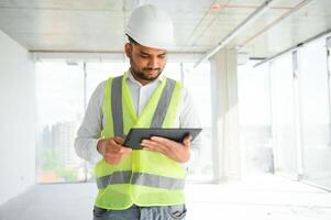 Indian construction site manager standing wearing helmet, thinking at construction site. Portrait of mixed race manual worker or architect photo