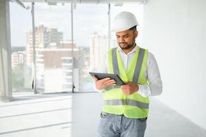Indian construction site manager standing wearing helmet, thinking at construction site. Portrait of mixed race manual worker or architect photo