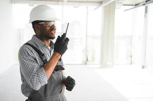 Builder in helmet is standing in front of the construction site, talking by walkie talkie control and communicate with worker photo