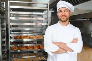 Happy baker standing near tray with bread at the bakery photo