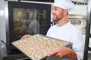 Young Caucasian worker in work wear holding tray with cookies photo