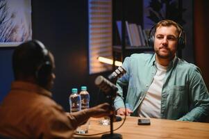 Man podcaster influencer blogger smiling while broadcasting his live audio podcast in studio using headphones. Male radio host making podcast or interview photo